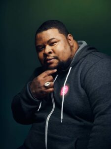 Michael Twitty wearing a dark gray hoodie resting his chin in his hand.