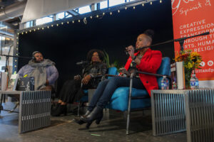 Three people seated on stage in front of microphones addressing and audience.