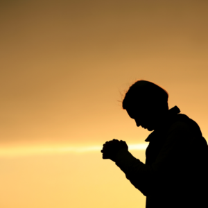 Person praying in profile backlit by a setting sun.